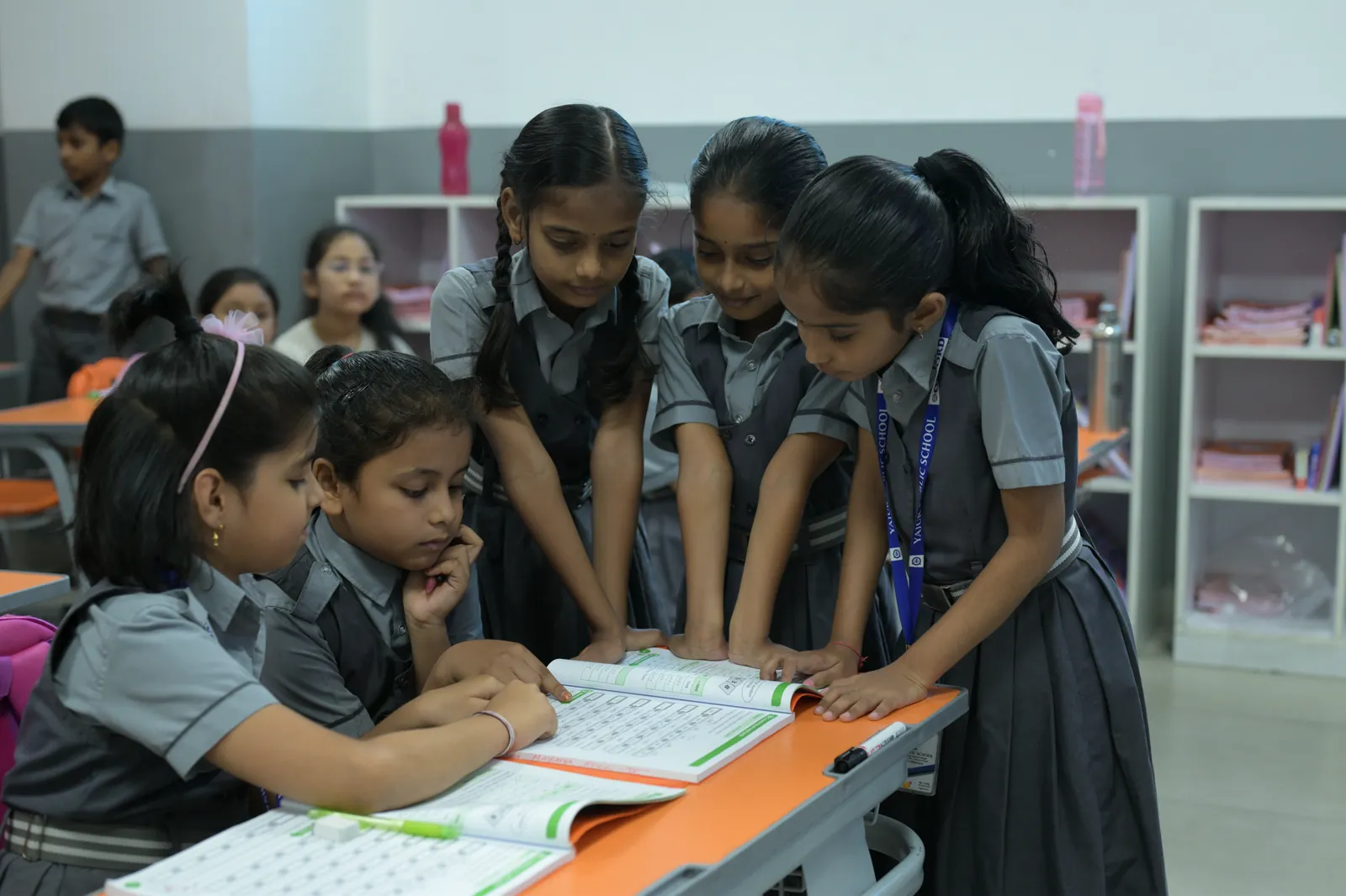 Six students crowded around one desk, working a problem out of a shared book between them