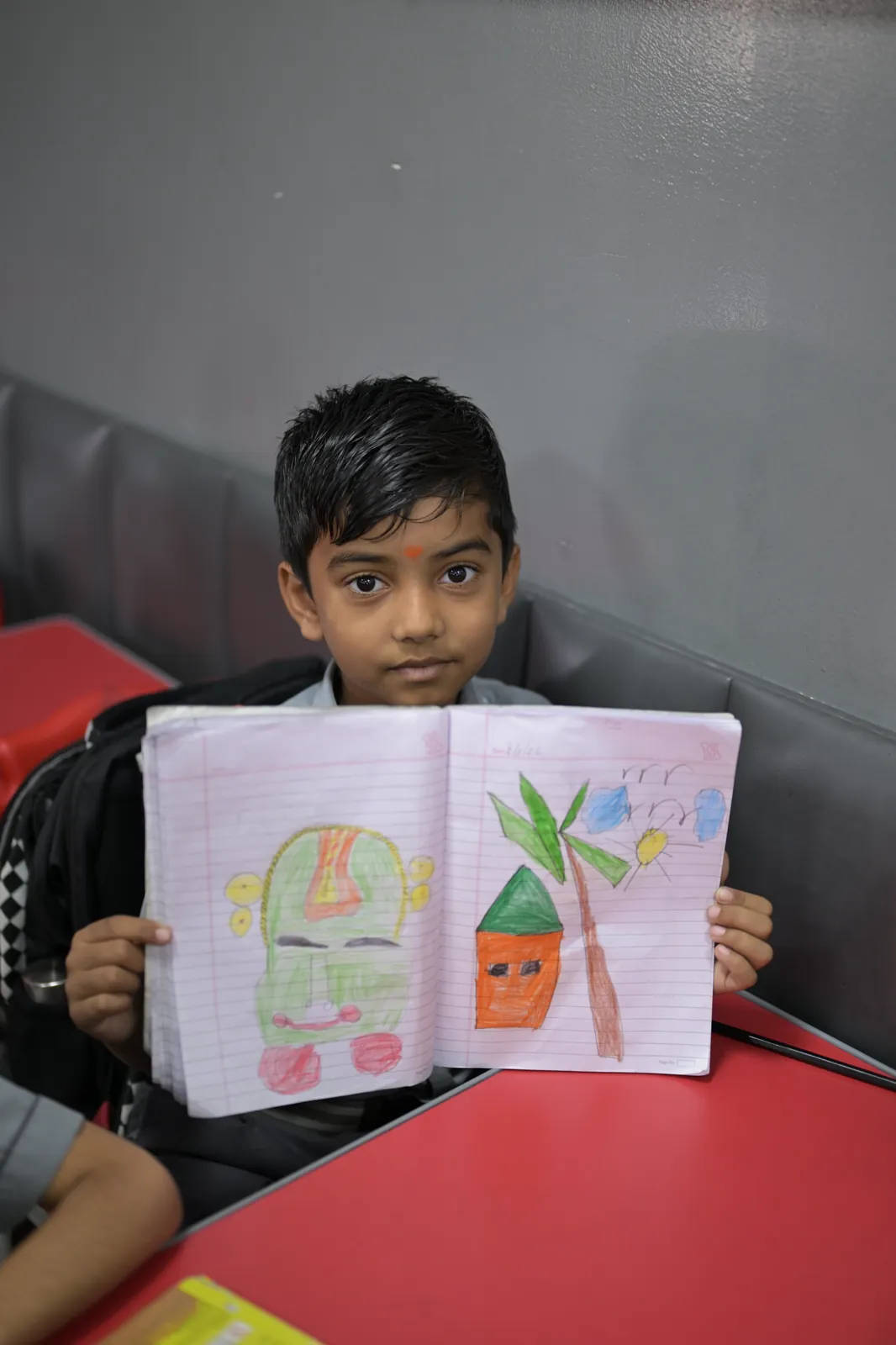 A student holding his notebook open to the camera to show the two drawings filling its pages.