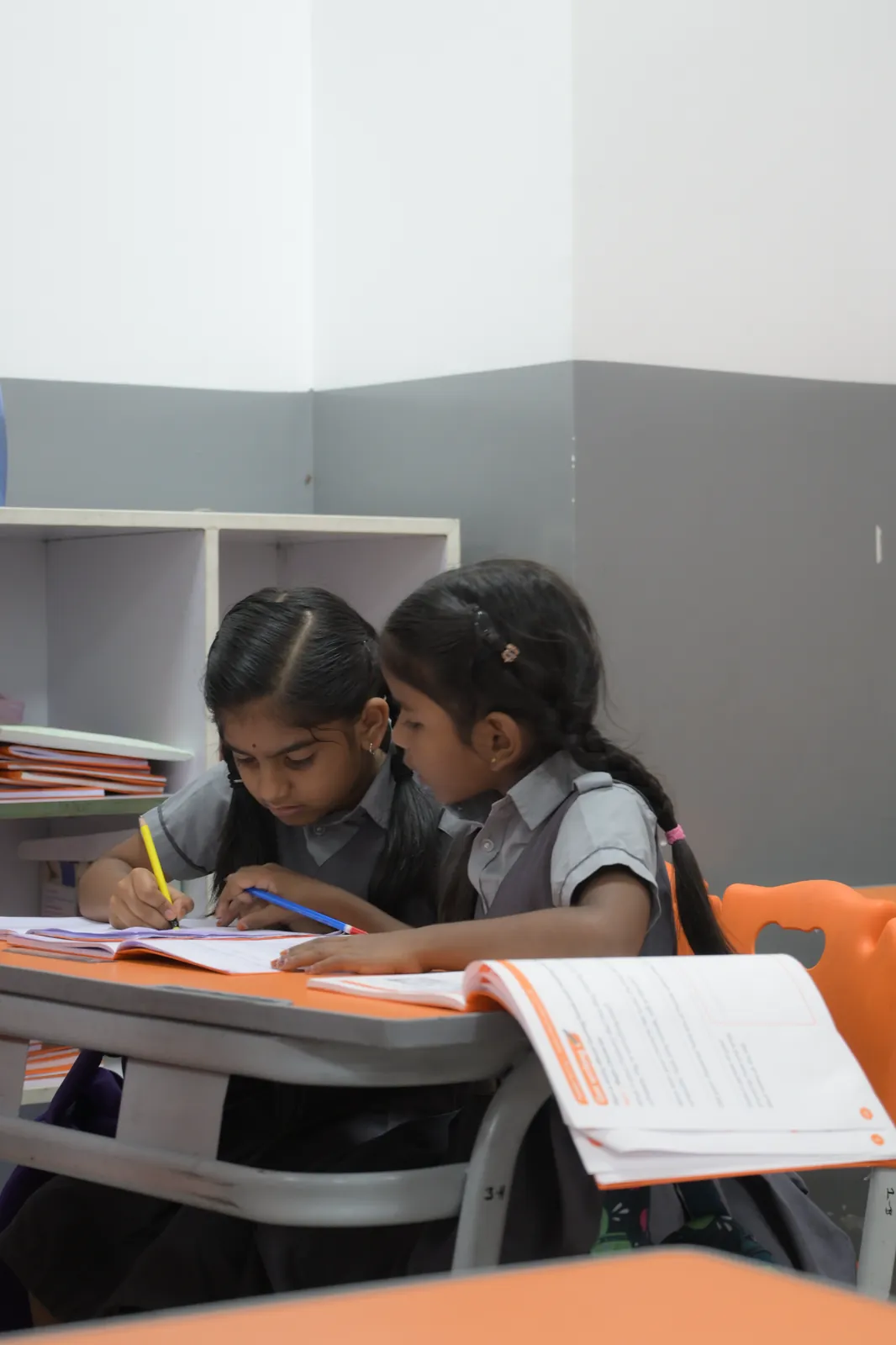 Two students sharing a desk, writing their way through the same worksheet side by side.