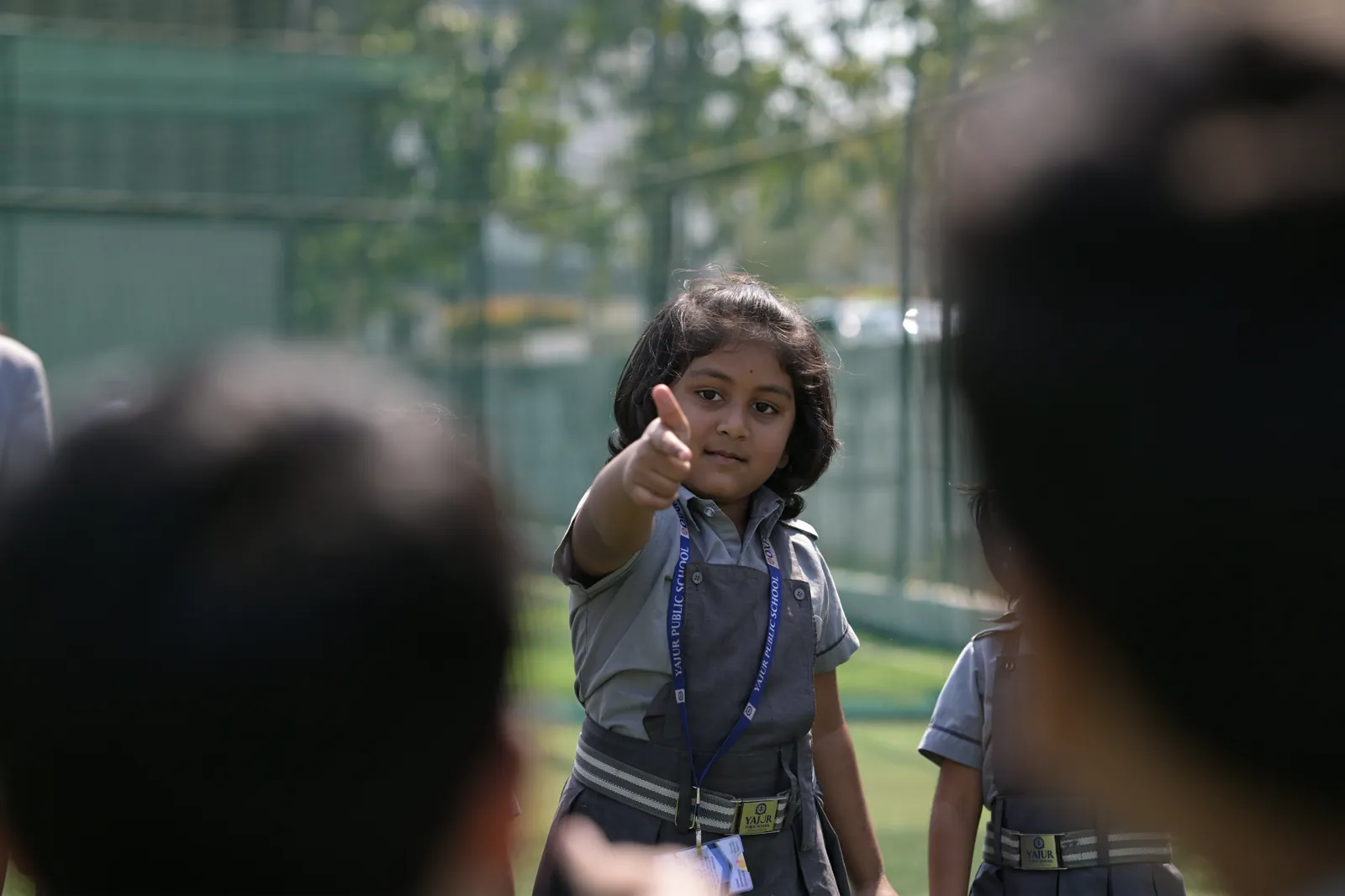 A student pointing across the circle to pick the next turn, her classmates blurred in the foreground.