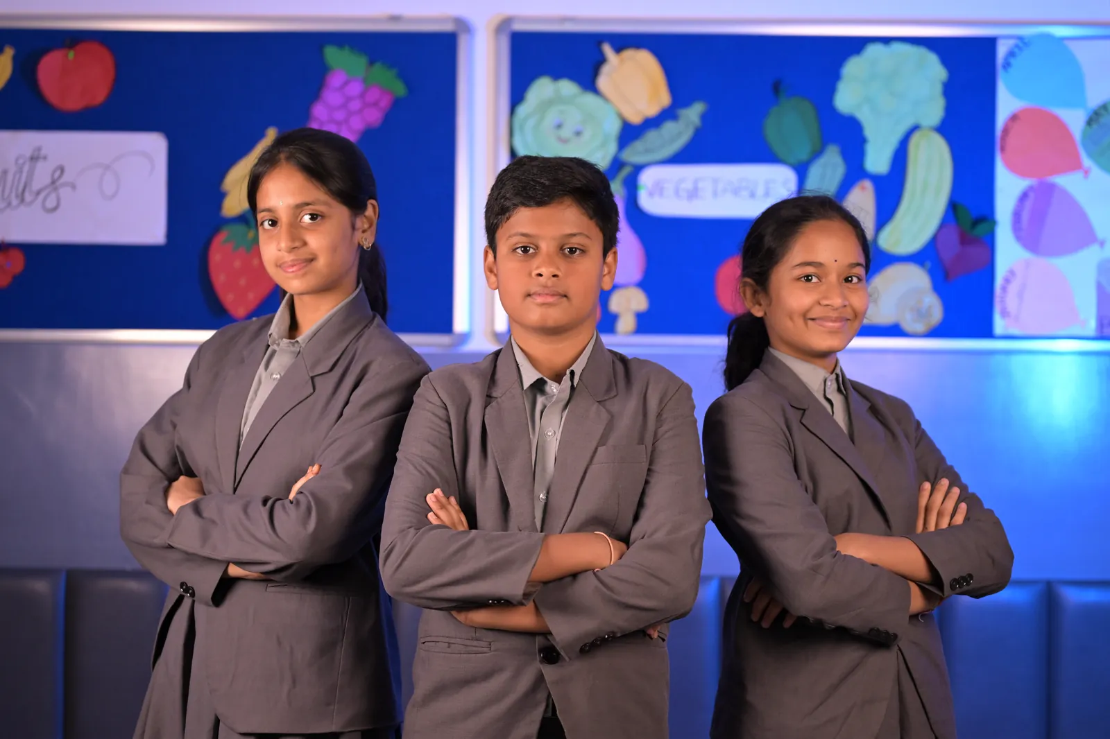 Three senior students in school blazers standing in front of a classroom display board.