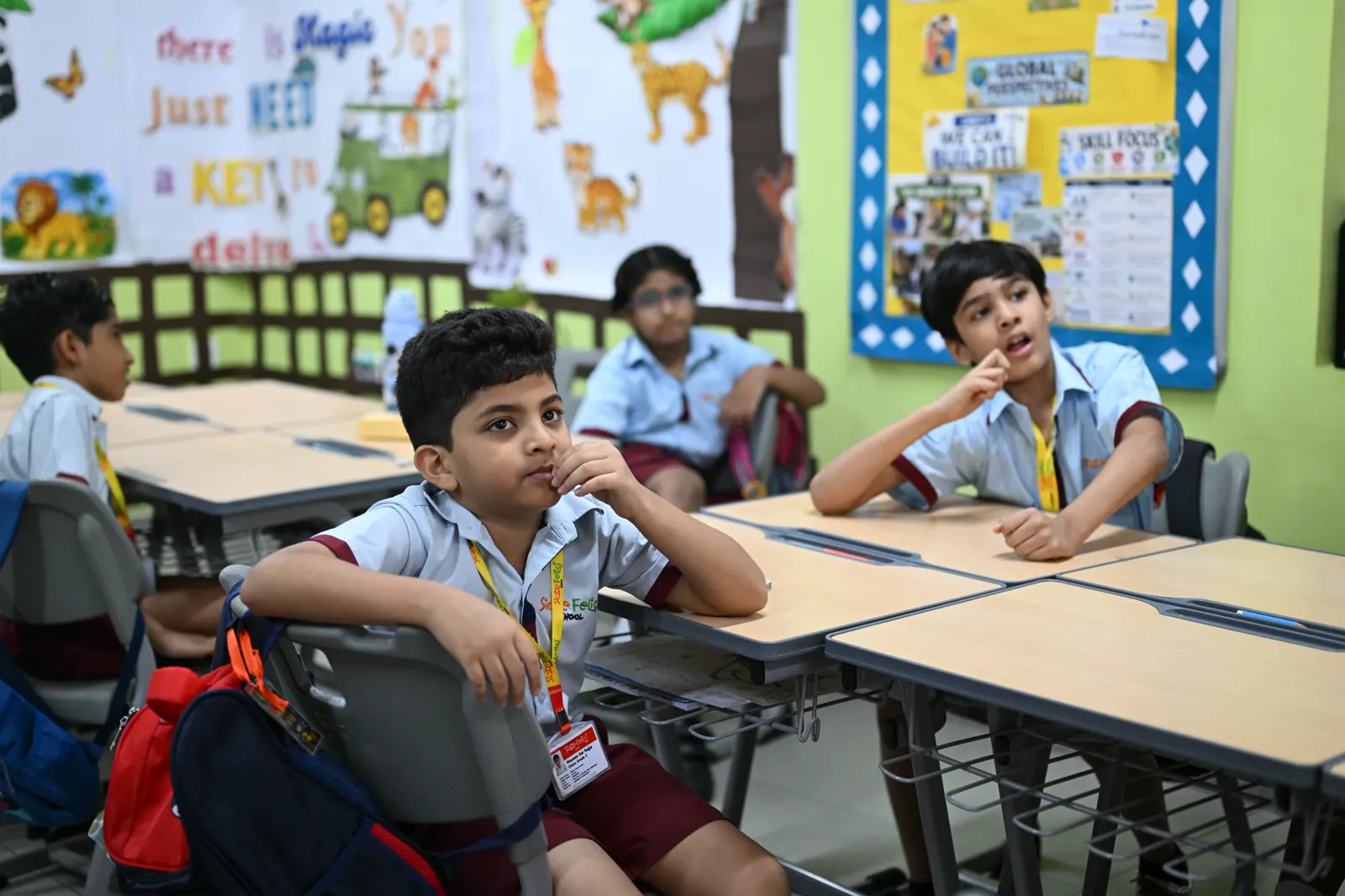 Primary-school students at their desks during a session, classroom skill-focus displays on the wall behind them.