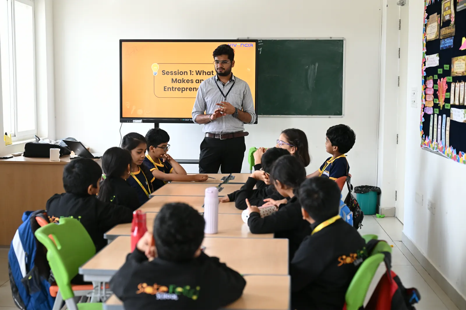 A Vivencia facilitator opening the first entrepreneurship session, the title slide on the classroom screen and students seated around joined tables.