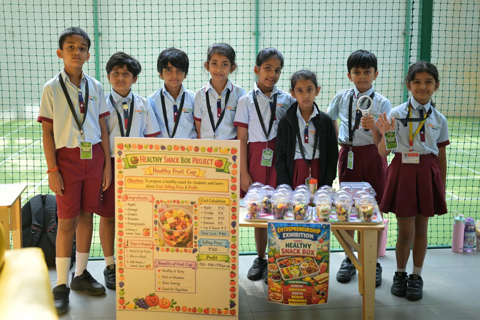 Seven students standing behind their Healthy Snack Box Project board and the packaged snacks they made to sell