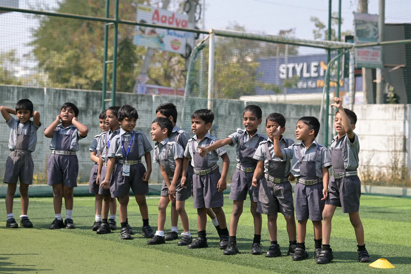 The youngest students lined up across the turf at the start of a games session, hands raised to their foreheads.